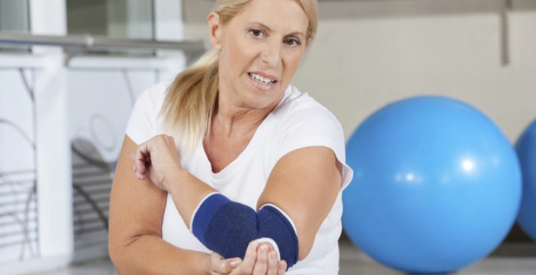 Elderly woman holding her aching elbow with bandage in gym