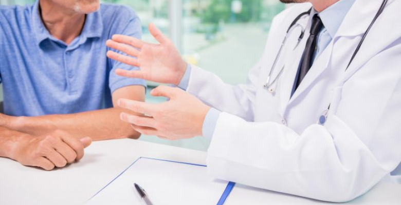 Male doctor talking with patient seriously at clinic. Close-up.