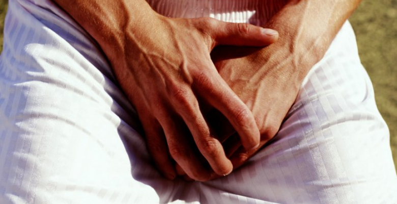 Man covering groin with hands, outdoors, close-up